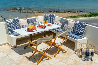a table and chairs on a patio with a view of the ocean at Beach House Kalamaki steps away from the beach in Galatás