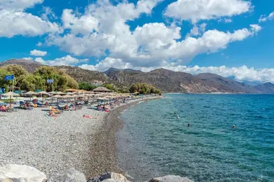a beach with umbrellas and people on the water at Erontas Apartment in Palaiochóra