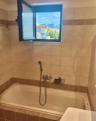 a bath tub with a shower in a bathroom with a window at Zoi’s Apartment in Chania Town