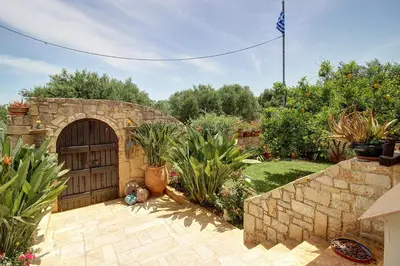 a stone building with a wooden door in a garden at Olive Villa Plataniás in Xirokámbion