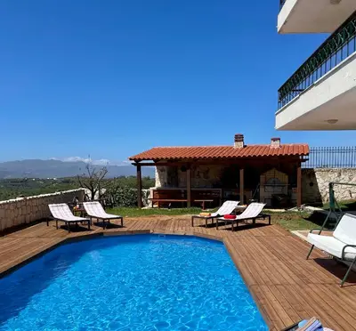 a swimming pool on a deck with chairs and a house at Olive Villa Plataniás in Xirokámbion