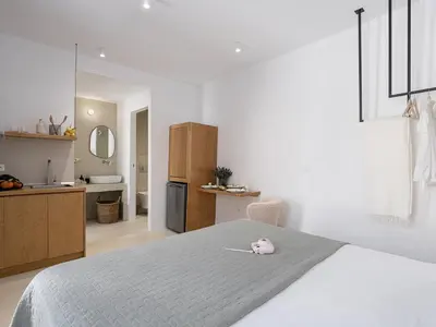 a white bedroom with a bed and a kitchen at Lithos Retreat 2(ΛΙTHOS Retreat) in Kolymvari