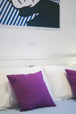a white bed with purple pillows and a picture above it at Origeo casa in Maleme