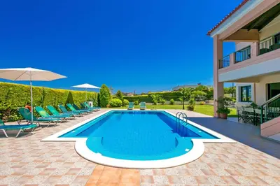 a villa with a swimming pool with chairs and an umbrella at Villa Margarita Exi by Villa Plus in Kalyves