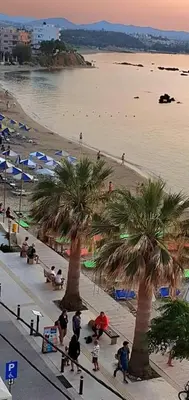 a beach with palm trees and people sitting on benches at Christina_Apt in Chania Town