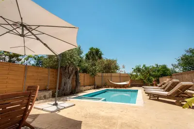 a swimming pool with an umbrella and chairs and a table at Avocado Villas in Chania Town