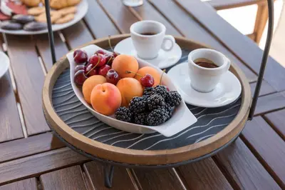 a plate of fruit on a table with cups of coffee at Nidus President in Souda