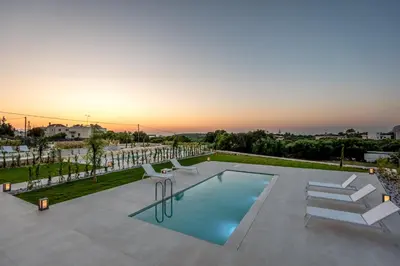 a pool with chairs and a sunset in the background at Efrossini Suites in Kounoupidhianá