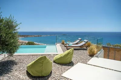 a swimming pool with two green chairs and the ocean at Krystallon Villas in Palaiochóra
