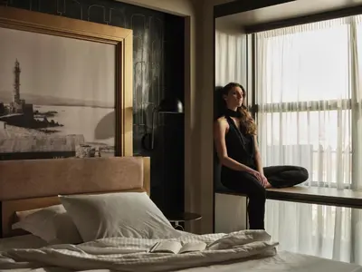 a woman sitting on a window sill next to a bed at The Chania Hotel Crete, Vignette Collection in Chania Town