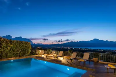 a pool with chairs and a view of the ocean at night at Caneva Luxury Villa in Tavronitis
