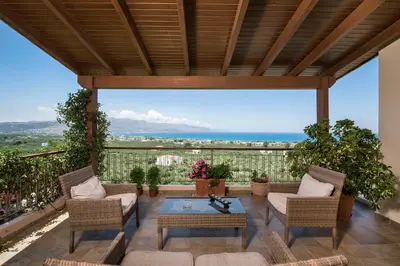 a patio with chairs and a table and a view of the ocean at Caneva Luxury Villa in Tavronitis