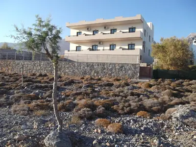 a building in the middle of a rocky field with a tree at Kritamos Beach Apartments in Frangokastello