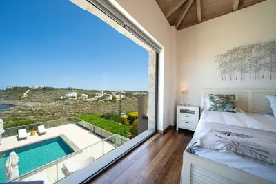 a bedroom with a large window and a swimming pool at Villa Poseidon One - Sunset & Sea Front Villa in Chorafakia