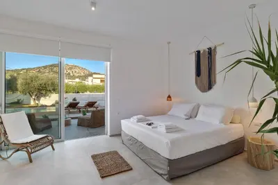 a white bedroom with a bed and a chair at Annassa Experience Villa 2' walk from Almyrida beach in Almirida