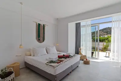 a white bedroom with a bed and a large window at Annassa Experience Villa 2' walk from Almyrida beach in Almirida