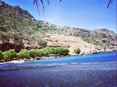 a beach with blue water and a mountain at Orea Kaliva in Sfinárion