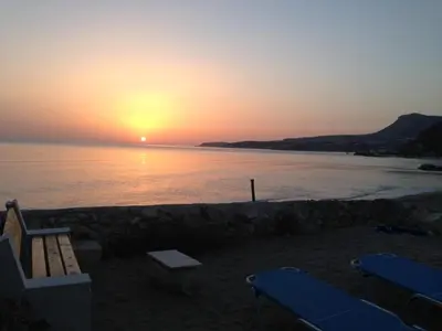 a sunset on a beach with two chairs and the ocean at Asterias Studios & Apartments in Kalyves