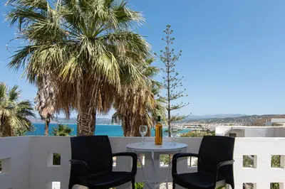a table with a glass of wine on a balcony with palm trees at Delfini Apartments in Kissamos