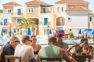 a group of people sitting at a table by a pool at Chrispy Waterpark Resort - All inclusive in Kolymvari
