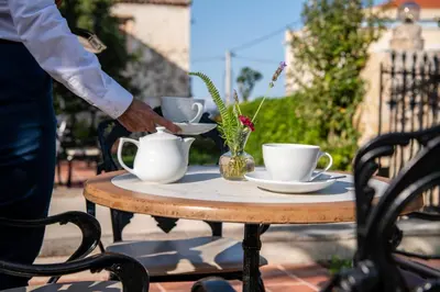 a person is pouring tea into cups on a table at Halepa Hotel in Chania Town