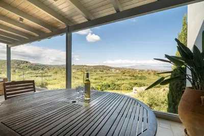 a bottle of wine sitting on a wooden table in front of a window at Villa Lucy by PosarelliVillas in Plataniás