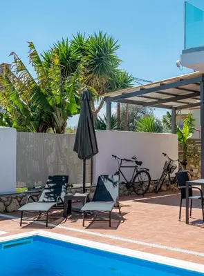 a swimming pool with chairs and an umbrella and bikes at Villa Meltemi in Daratso