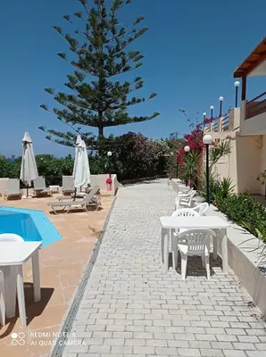 a patio with tables and chairs next to a tree at Alexandros Studios in Kalamaki Chanion