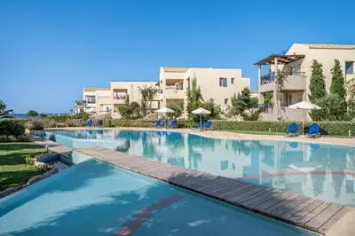 a large swimming pool with blue chairs and buildings at Calmaliving Seaside apartments with pool in Gerani Chanion