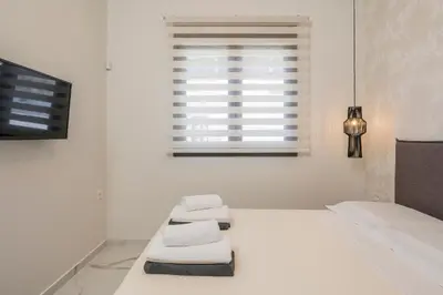 a white bedroom with a bed and a window at Orama Luxury Apartments in Agia Marina Nea Kydonias