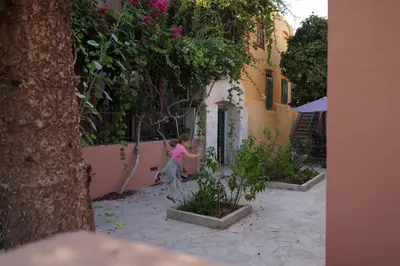 a little girl is sitting in a garden next to a building at Lindas Convent Garden Home 1 in Chania Town