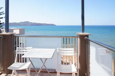 a table and chairs on a balcony overlooking the ocean at Cozy Corner VS Beachfront in Stalos