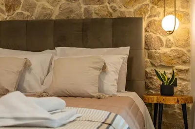 a bed with white pillows and a stone wall at Casa Dionysia - New Lux 2Br with Jacuzzi near Maleme Beach in Maleme